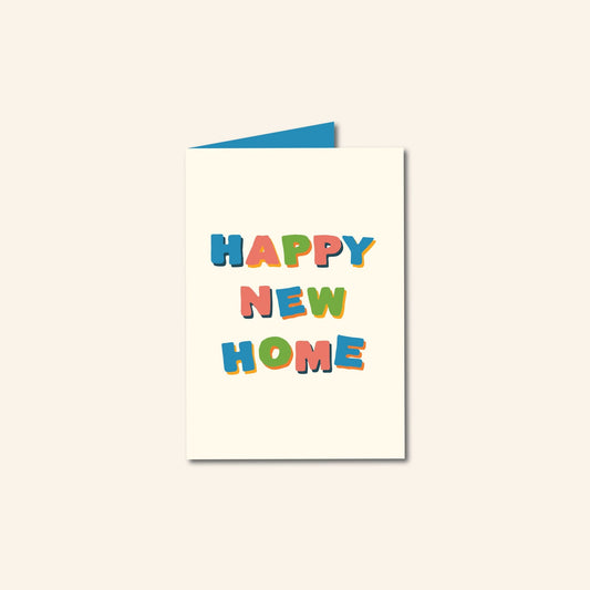 Wenskaart met de tekst “HAPPY NEW HOME” in kleurrijke, speelse letters op een crèmekleurige achtergrond, met een kraft envelop en een blauwe binnenkaart – illustratief ontwerp van Studio Bloos.