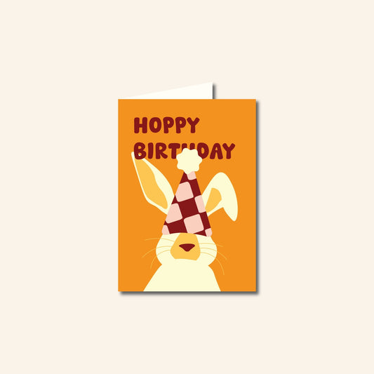 Wenskaart Hoppy Birthday met een illustratie van een konijn met feestmuts en vrolijke tekst, originele verjaardagskaart van Studio Bloos.