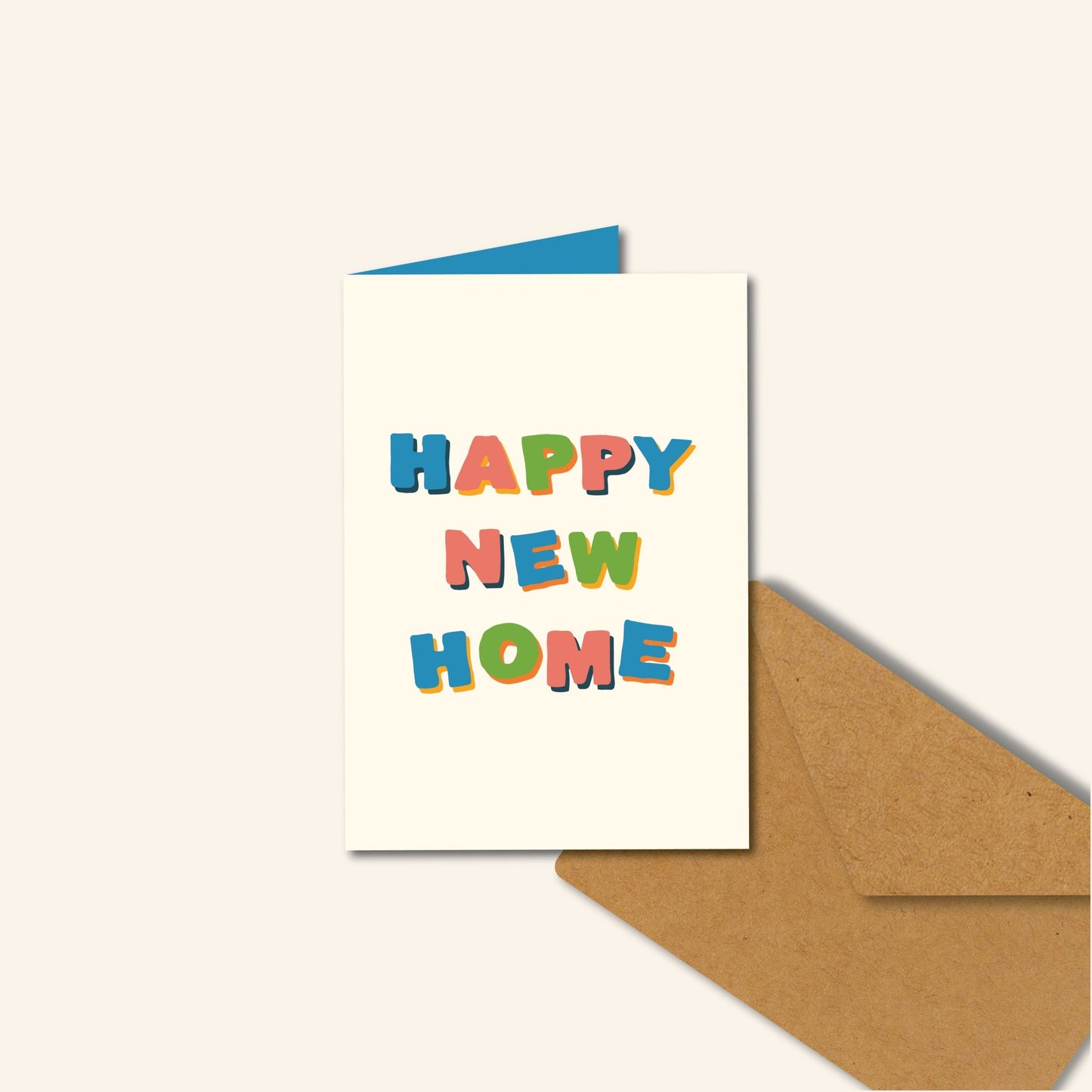 Wenskaart met de tekst “HAPPY NEW HOME” in kleurrijke, speelse letters op een crèmekleurige achtergrond, met een kraft envelop en een blauwe binnenkaart – illustratief ontwerp van Studio Bloos.